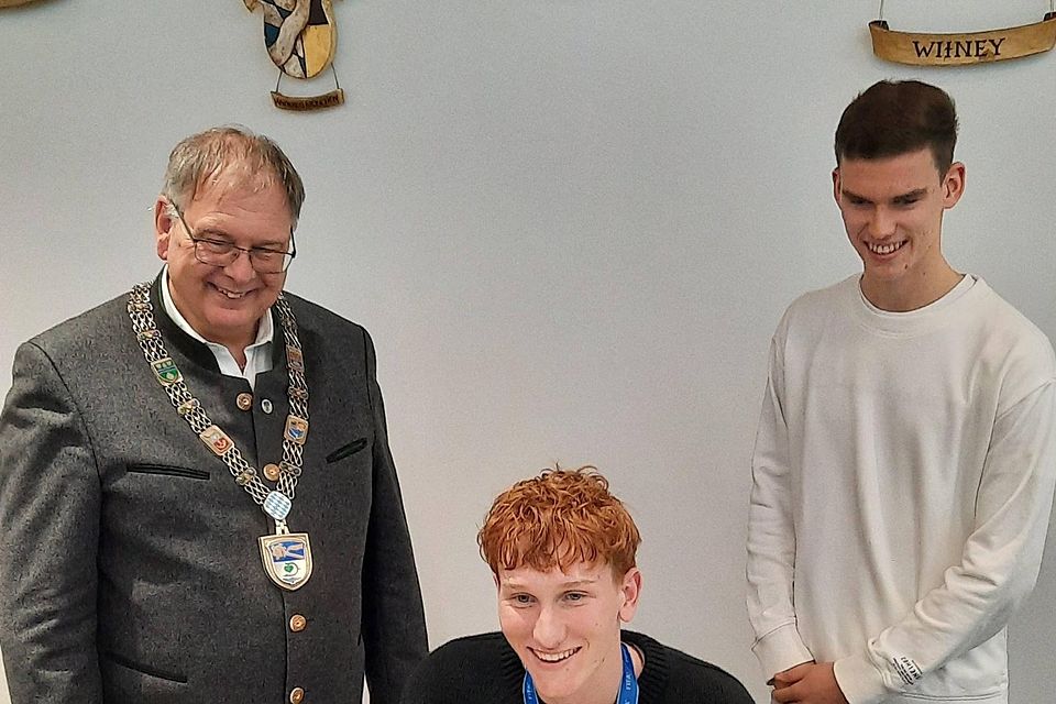 Konstantin Heide trägt sich ins goldene Buch der Gemeinde ein. Mitspieler Robert Ramsak hat es schon getan und Bürgermeister Wolfgang Panzer freut sich mit den beiden Fußballern.