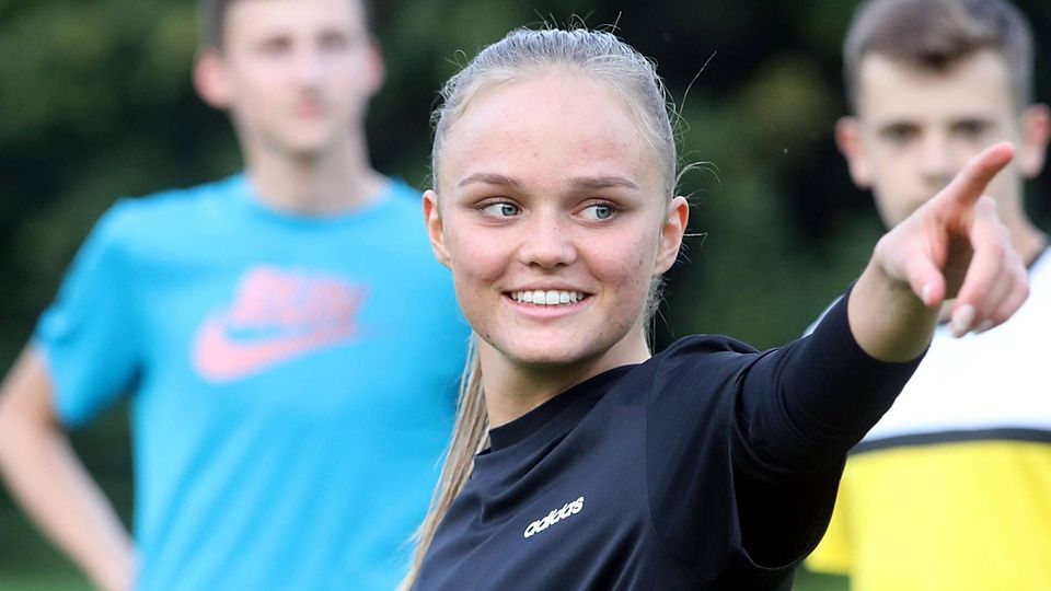Giselle Beylich deutet mit dem Finger nach rechts, im Hintergrund zwei Juniorenspieler des SE Freising.