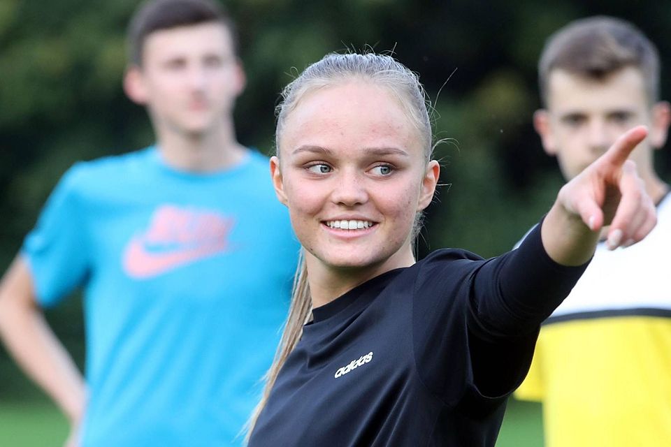 Giselle Beylich deutet mit dem Finger nach rechts, im Hintergrund zwei Juniorenspieler des SE Freising.