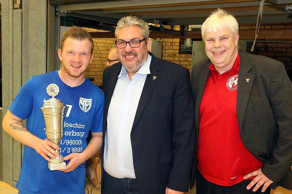Entspanntes Lächeln: Marcel Strubel vom FCO II (von links) nimmt den Pokal für den Turnierzweiten entgegen, Bürgermeister Achim Wilmsmeier und SuS-Vorsitzender Michael Grützkowski gratulieren.