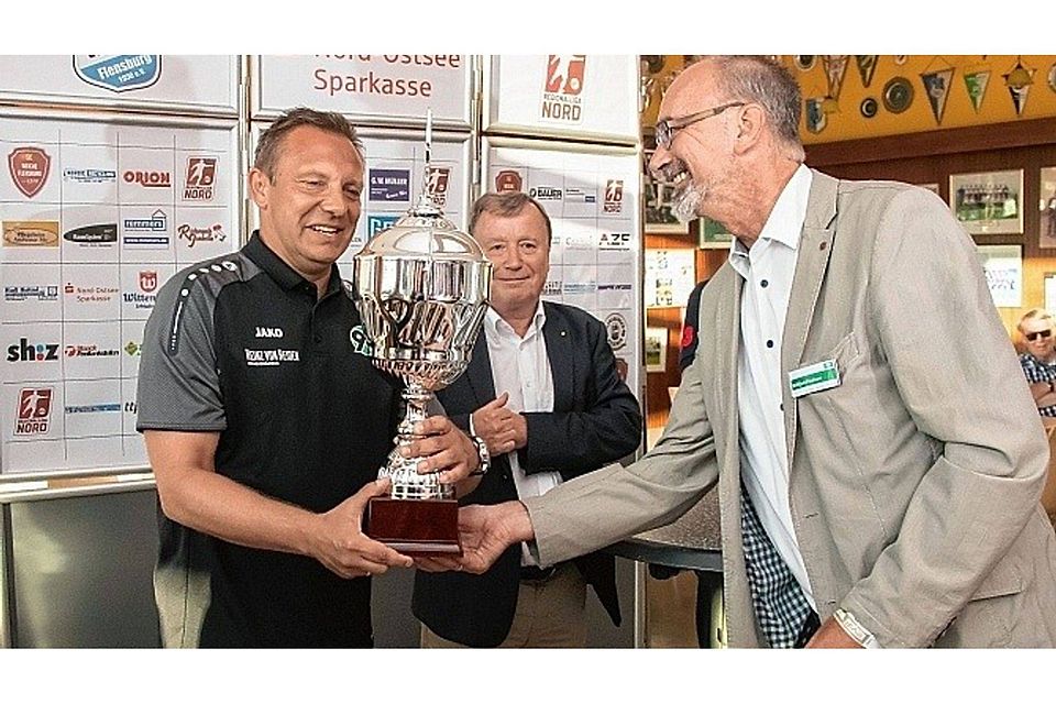 Bitteschön! Winfried Paulsen (re.) überreicht den „AOK-Cup“ an André Breitenreiter. Im Hintergrund der stellvertretende sh:z-Chefredakteur Jürgen Muhl.