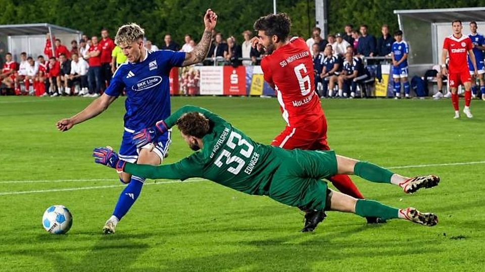 Schott-Torjäger Gianni Auletta (blaues Trikot) hat hier im Verbandspokal-Achtelfinale das 4:0 auf dem Fuß, aber Hüffelsheims Keeper Tobi Edinger macht sich lang und pariert. Sein Teamkollege Sascha Mockenhaupt muss nicht mehr eingreifen. 	Foto: Mario Luge