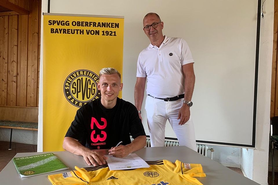 Benedikt Kirsch (vorne) unterzeichnet im Beisein von Geschäftsführer Wolfgang Gruber einen Vertrag bei der SpVgg Bayreuth.