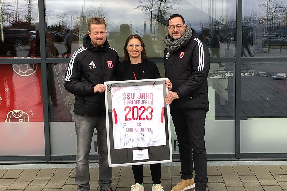 Christian Duschner (links) und Thomas Diertl (rechts) vom SC Luhe-Wildenau nehmen ein Trikot des SSV Jahn Regensburg von Jahn-Vertreterin Maike Lehner entgegen. 