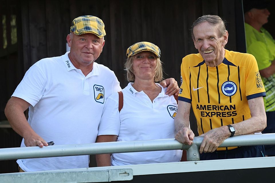 Auf dem Foto sind Stefan, Conny und der Ehrenpräsident des FC Pipinsried, Konrad Höß – im  Brighton-Dress – zu sehen.