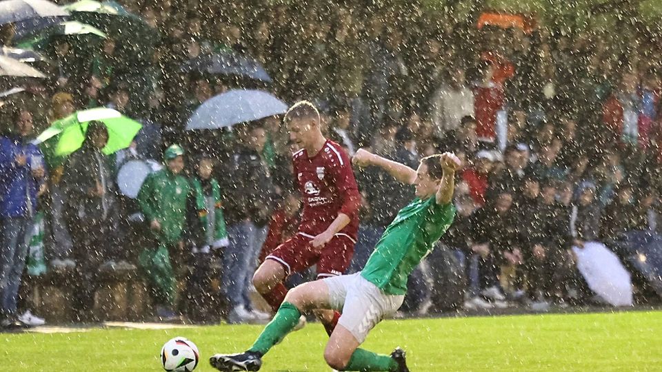 Englisches Wetter, englische Härte: Emmerings Verteidiger Georg Hanslmayer (grün) grätscht den Angriffsversuch von Schnaitsees Lukas Wastlhuber sauber ab – dem grün-weißen Anhang gefällt‘s.