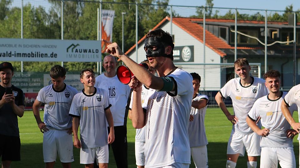 Die Maske, die er wegen einer schweren Gesichtsverletzung trägt, ist so etwas wie sein Markenzeichen geworden: „Setz sie auf, setz sie auf“, riefen die TuS-Fußballer, bevor sich ihr Kapitän Sebastian Schrills per Megafon bei den Fans bedankte.