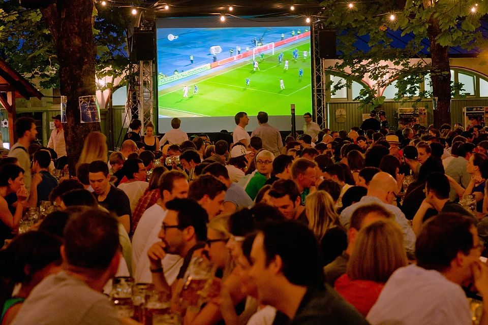 Fußballfans schauen ein WM-Spiel im Biergarten auf Großleinwand.