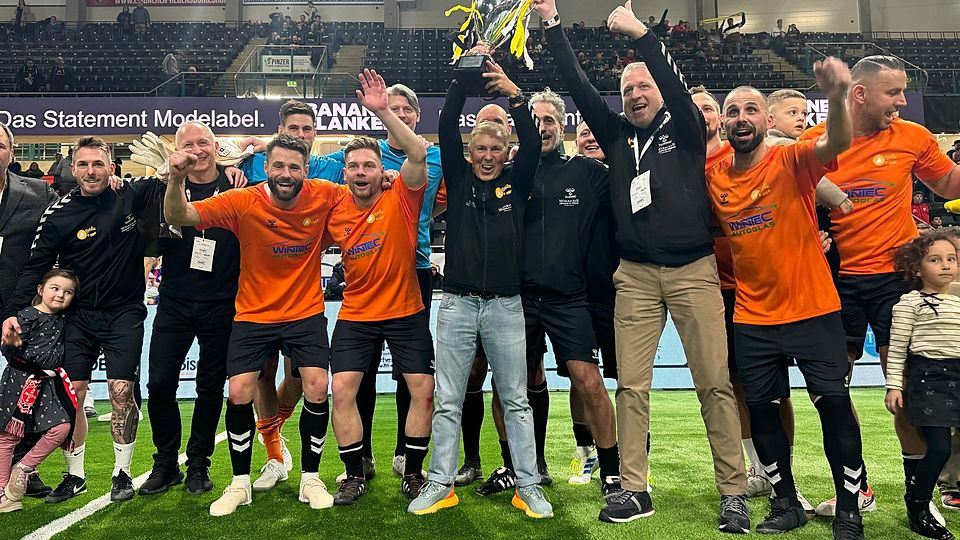 Coach Jürgen Press und Manager Andy Mühlbauer stemmen den Pokal für das Siegerteam von Balu4Kids in die Höhe.