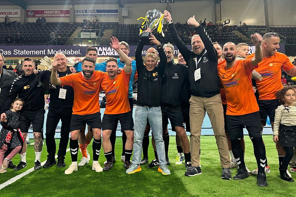 Coach Jürgen Press und Manager Andy Mühlbauer stemmen den Pokal für das Siegerteam von Balu4Kids in die Höhe.